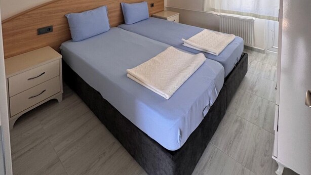 A double bed with a wooden headboard, a bedside table, and a nightstand. - Orçın Apartmanı (Lapseki)