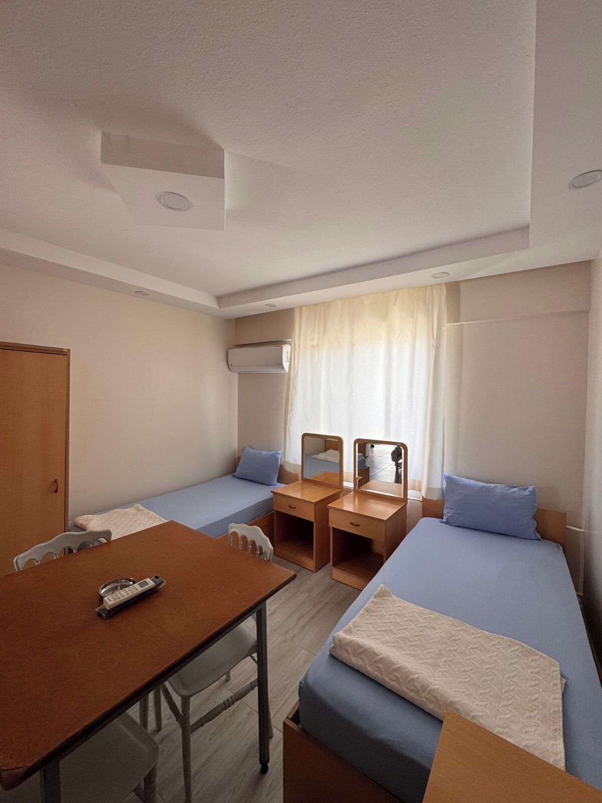 Habitación de hotel compacta con dos camas individuales, un escritorio pequeño con silla, una mesita de madera y un teléfono.