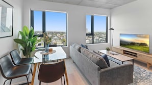 A modern living room with a glass dining table, two sofas, a TV, and large windows offering city views. - Sophisticated 2-bed With Bay Views & Amenities (Melbourne)