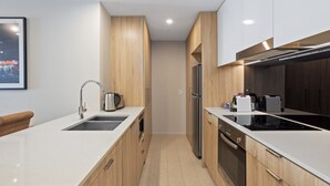 A modern kitchen with wooden cabinets, a stainless steel refrigerator, and a black induction cooktop. - Cosy 1-bed With River Views, Pool, Gym & BBQ (Brisbane)