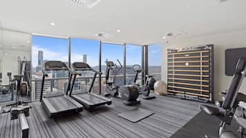 A modern gym with treadmills, elliptical machines, and weight equipment, large windows with a city view.