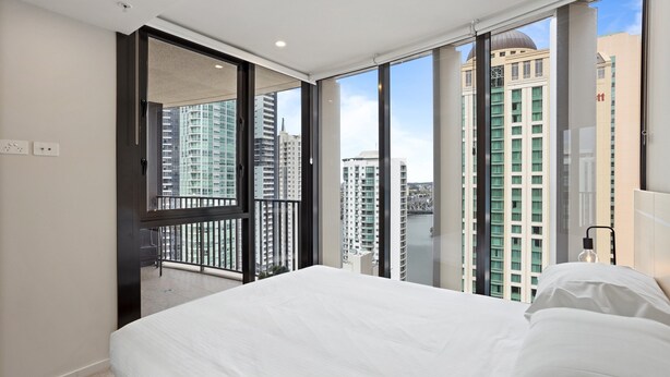 A bedroom with a large bed, a sliding glass door to a balcony, and a city view. - Cosy 1-bed With River Views, Pool, Gym & BBQ (Brisbane)