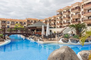 A swimming pool with a wooden bridge, surrounded by a resort building with balconies and outdoor seating. - Vacation Home 'Casa Marley – Balcòn Del Mar' with Shared Pool, Balcony and Wi-Fi (costa del Silencio)