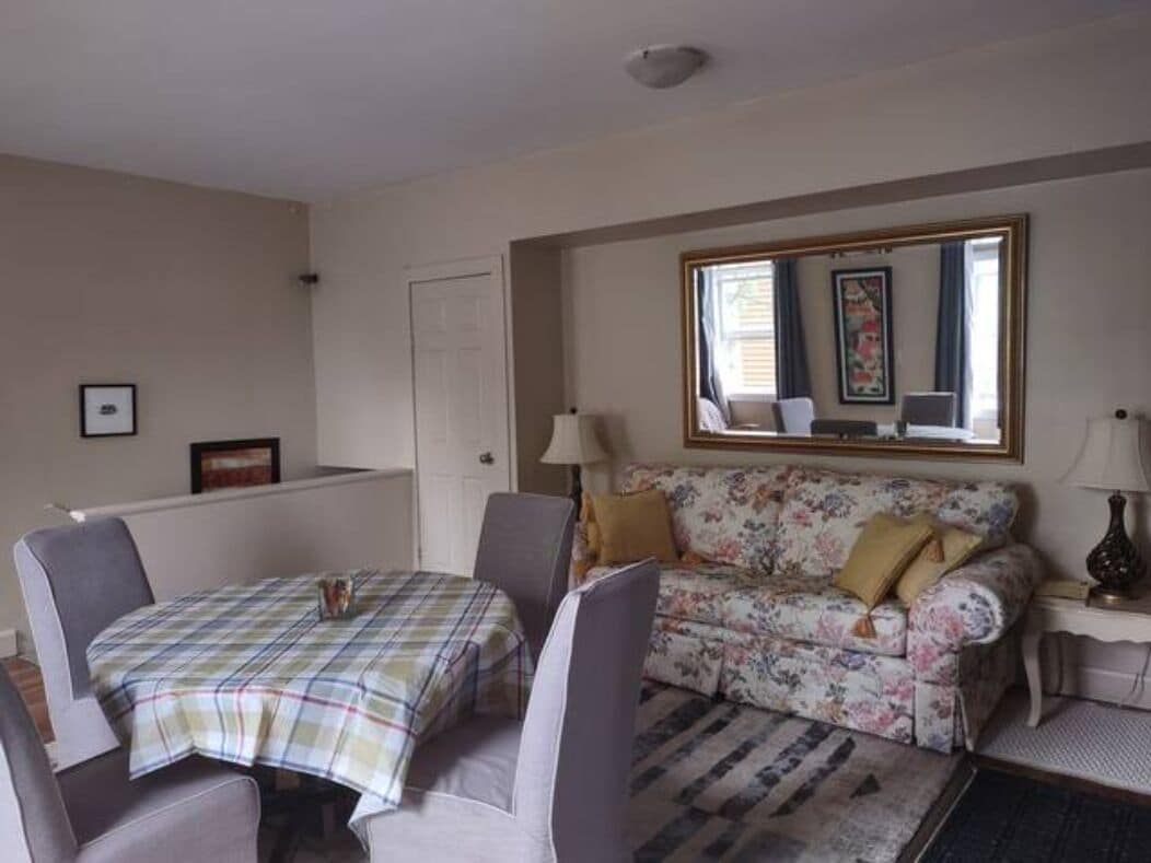 A room with a dining table and chairs, a floral sofa, a mirror, and a lamp.