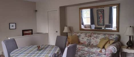 A room with a dining table and chairs, a floral sofa, a mirror, and a lamp.
