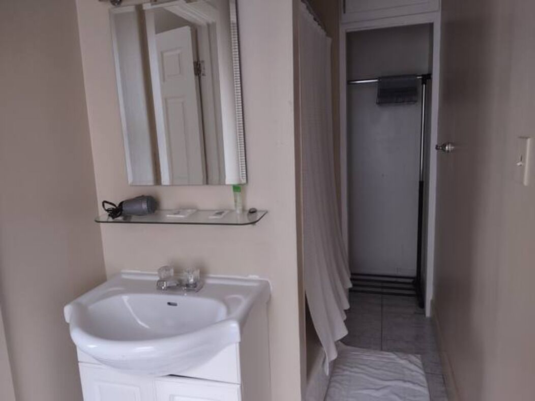 A bathroom with a white sink, a mirror above it, and a shower area with a towel hanging on the door.