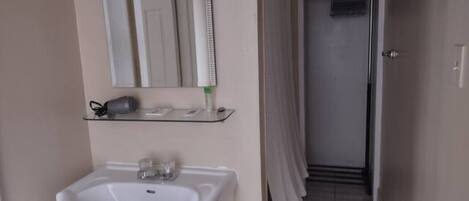 A bathroom with a white sink, a mirror above it, and a shower area with a towel hanging on the door.