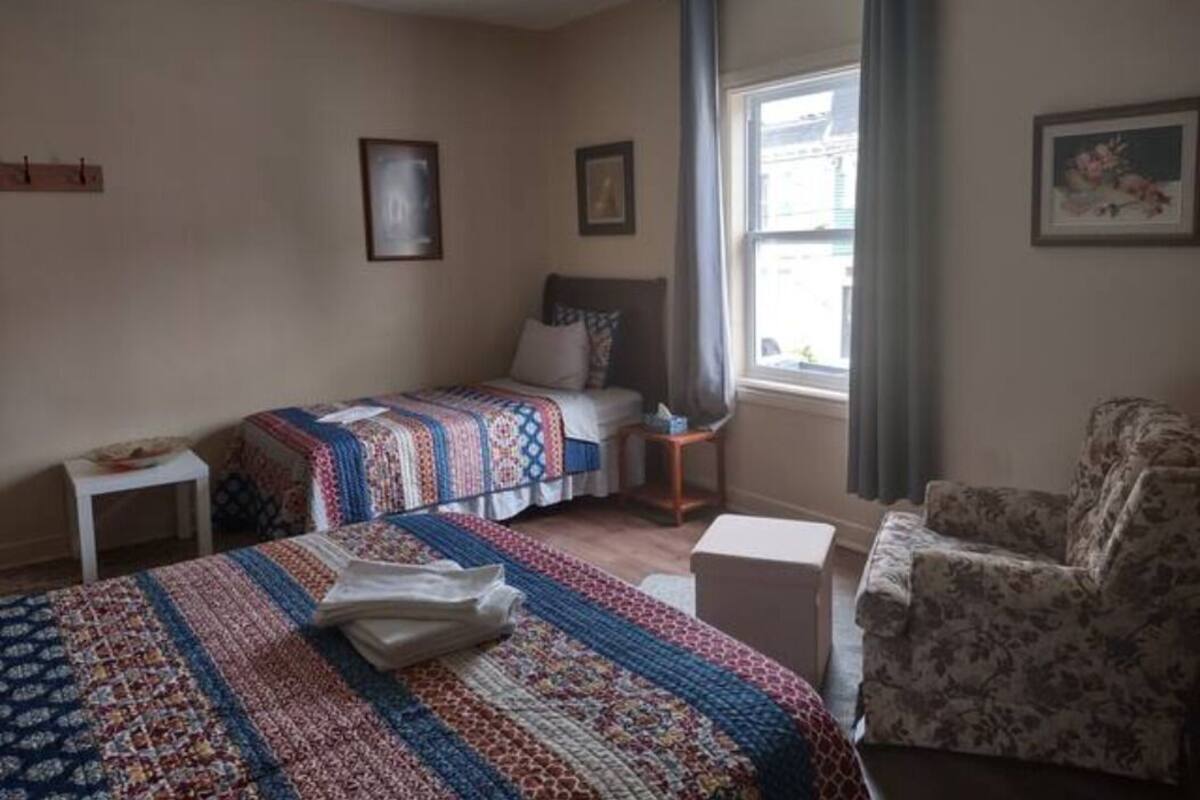 Une chambre avec deux lits, une chaise, une petite table et une fenêtre avec des rideaux.