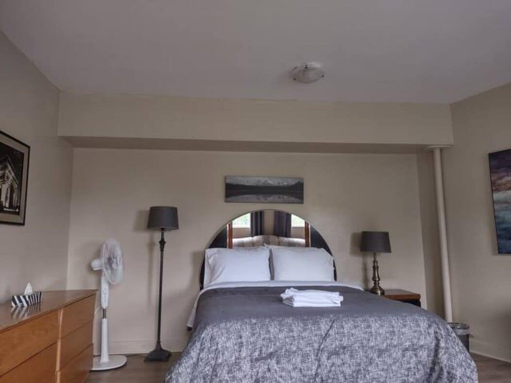 A bedroom with a bed, bedside lamps, a floor lamp, a fan, and a dresser.
