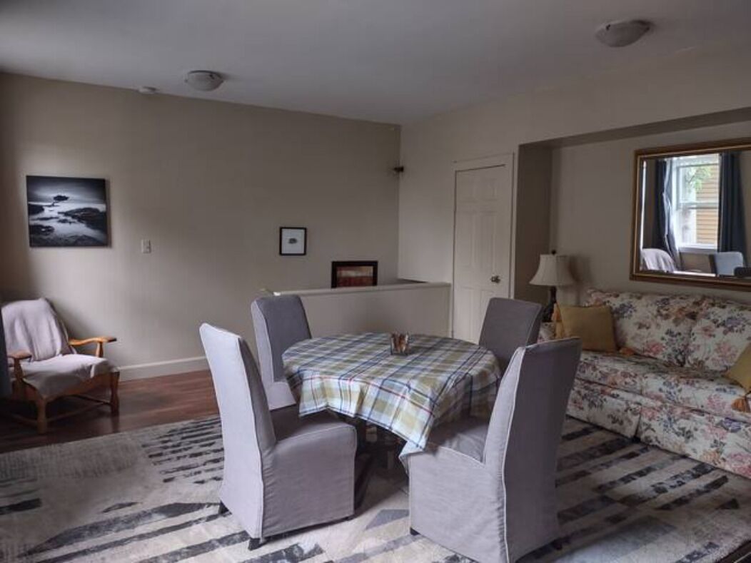 A living room with a plaid table, grey armchairs, a floral sofa, a rug, and a framed picture on the wall.