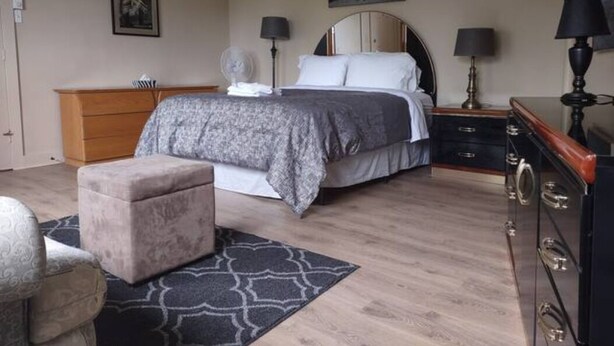 Un dormitorio con cama, mesitas de noche, cómoda, silla y alfombra.