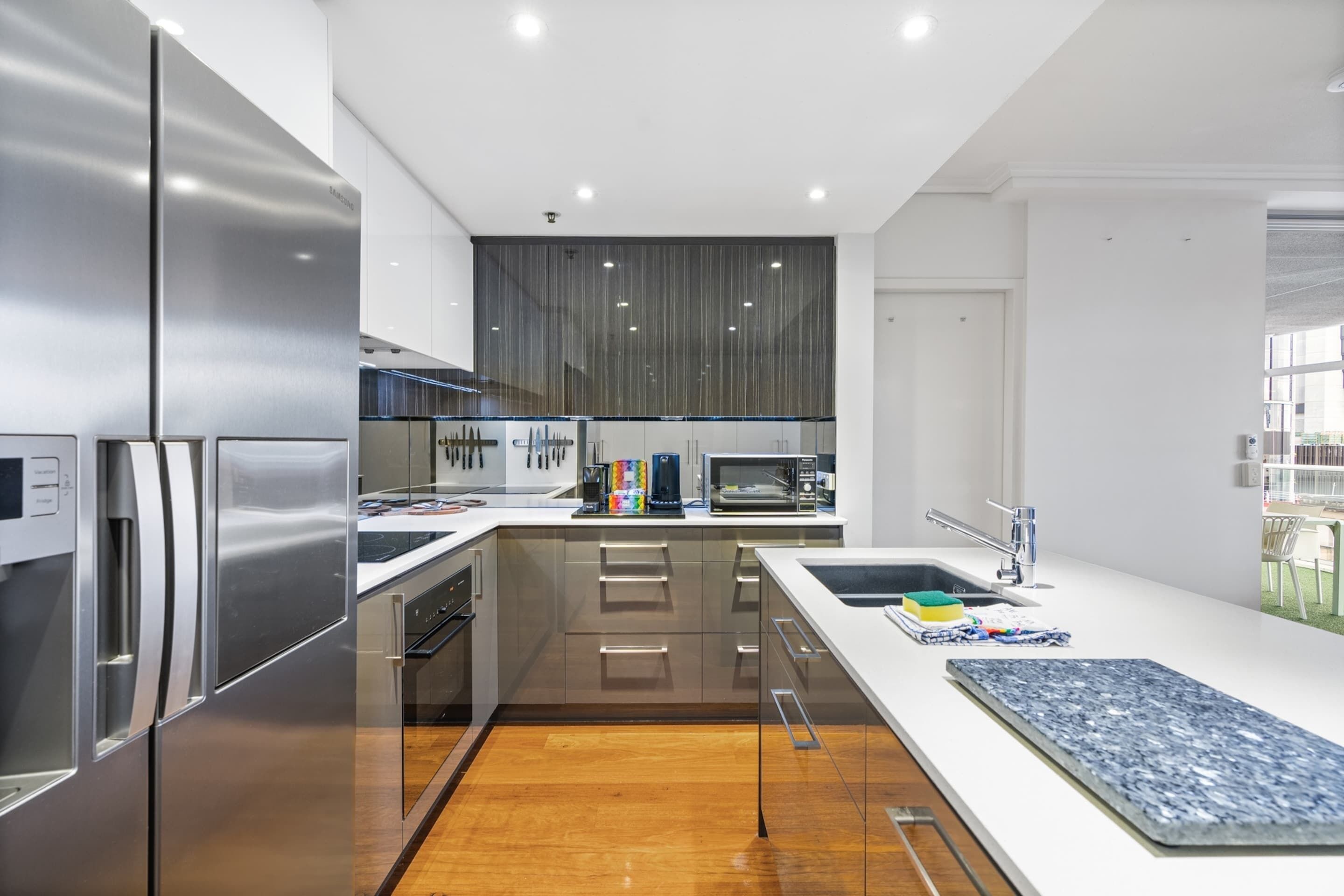 Una cocina moderna con electrodomésticos de acero inoxidable, piso de madera y una isla grande con fregadero.