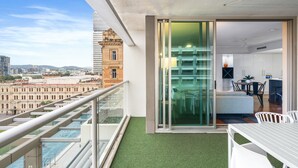 Un appartement moderne doté d’un balcon donnant sur le paysage urbain, comprenant un coin repas et une porte-fenêtre coulissante qui ouvre sur l’espace de vie.