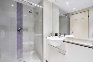 Un bagno moderno con cabina doccia in vetro, lavandino bianco e uno specchio grande.