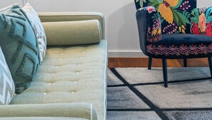 Une pièce comprenant un canapé, un fauteuil, une lampe et une fenêtre donnant sur un paysage urbain.