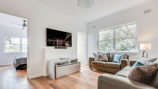 A modern living room with a flat-screen TV, leather sofas, and a large window. - Art Deco 2-bed Close to City and Harbour (Sydney)