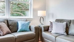 A modern living room with two leather sofas, a small side table with a lamp, and a large window with a view of trees. - Art Deco 2-bed Close to City and Harbour (Sydney)