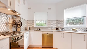 A modern kitchen with white cabinets, a stainless steel stove, a dishwasher, and a window with a view of greenery. - Art Deco 2-bed Close to City and Harbour (Sydney)