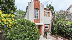 A modern two-story house with a brick facade, a small front porch, and a garden with various plants and flowers. - Art Deco 2-bed Close to City and Harbour (Sydney)