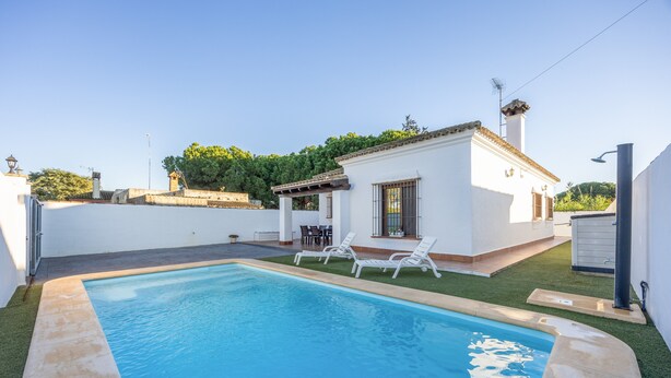 A swimming pool with lounge chairs, a patio area, and a small building with a tiled roof. - Holiday Home "Brisa Marina" with Private Pool, Wi-Fi and Air Conditioning (Chiclana de la Frontera)