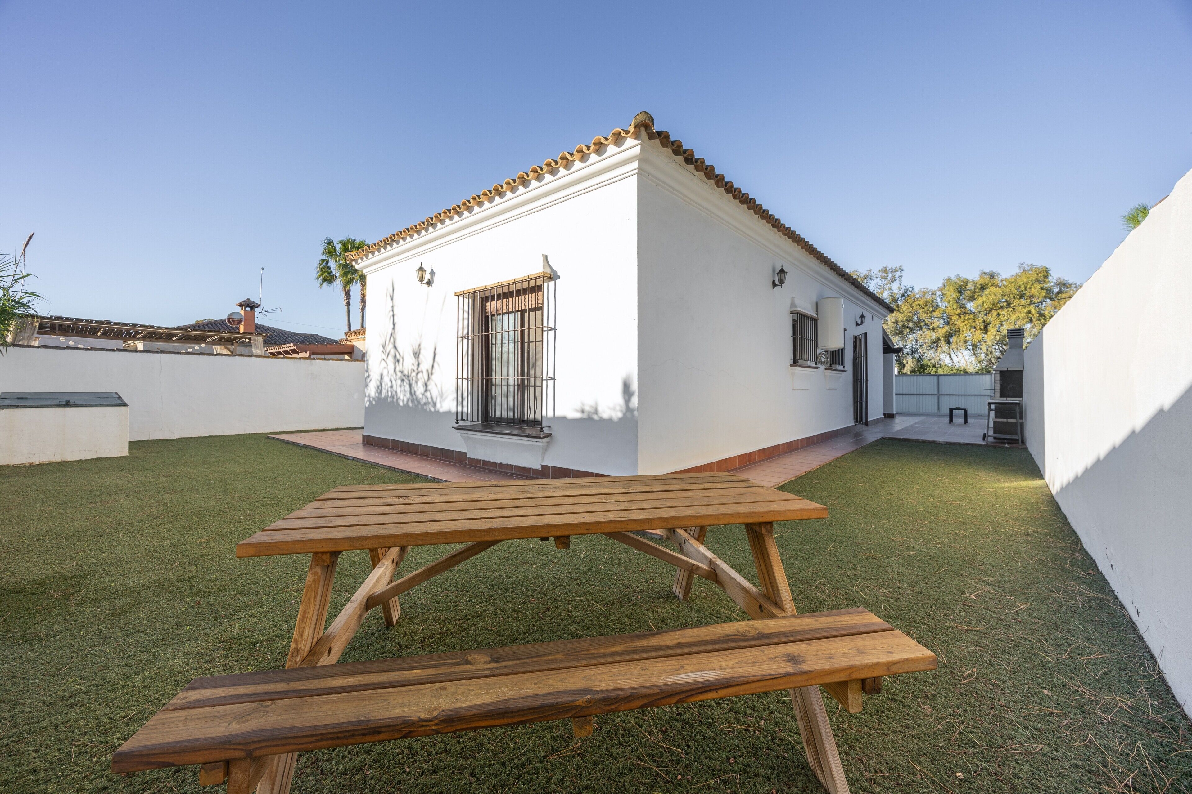 Un edificio blanco con tejado de baldosas, un banco de madera y un pequeño patio.