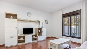 A modern living room with a TV, white cabinets, a wooden shelf, a bench, and a large window with a view. - Holiday Home "Brisa Marina" with Private Pool, Wi-Fi and Air Conditioning (Chiclana de la Frontera)