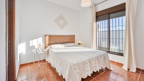 A bedroom with a bed, a nightstand, a wall-mounted decorative piece, and a window with curtains. - Holiday Home "Brisa Marina" with Private Pool, Wi-Fi and Air Conditioning (Chiclana de la Frontera)