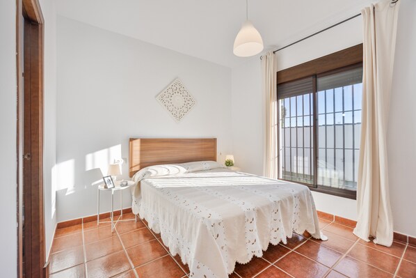 Une chambre à coucher comprenant un lit, une table de chevet, un élément décoratif fixé au mur et une fenêtre avec des rideaux.