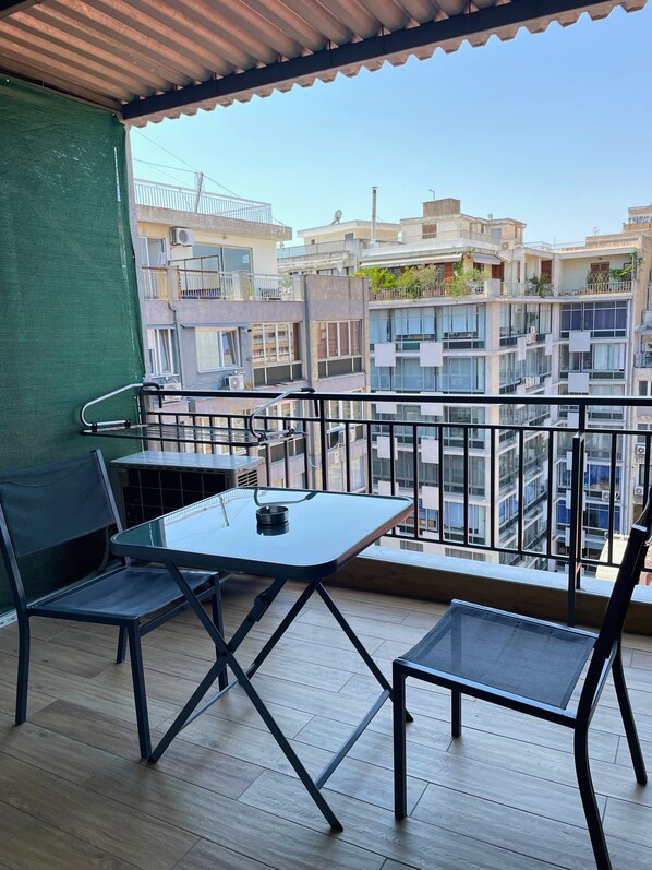 A balcony with a table and chairs, overlooking a residential area with multiple buildings.