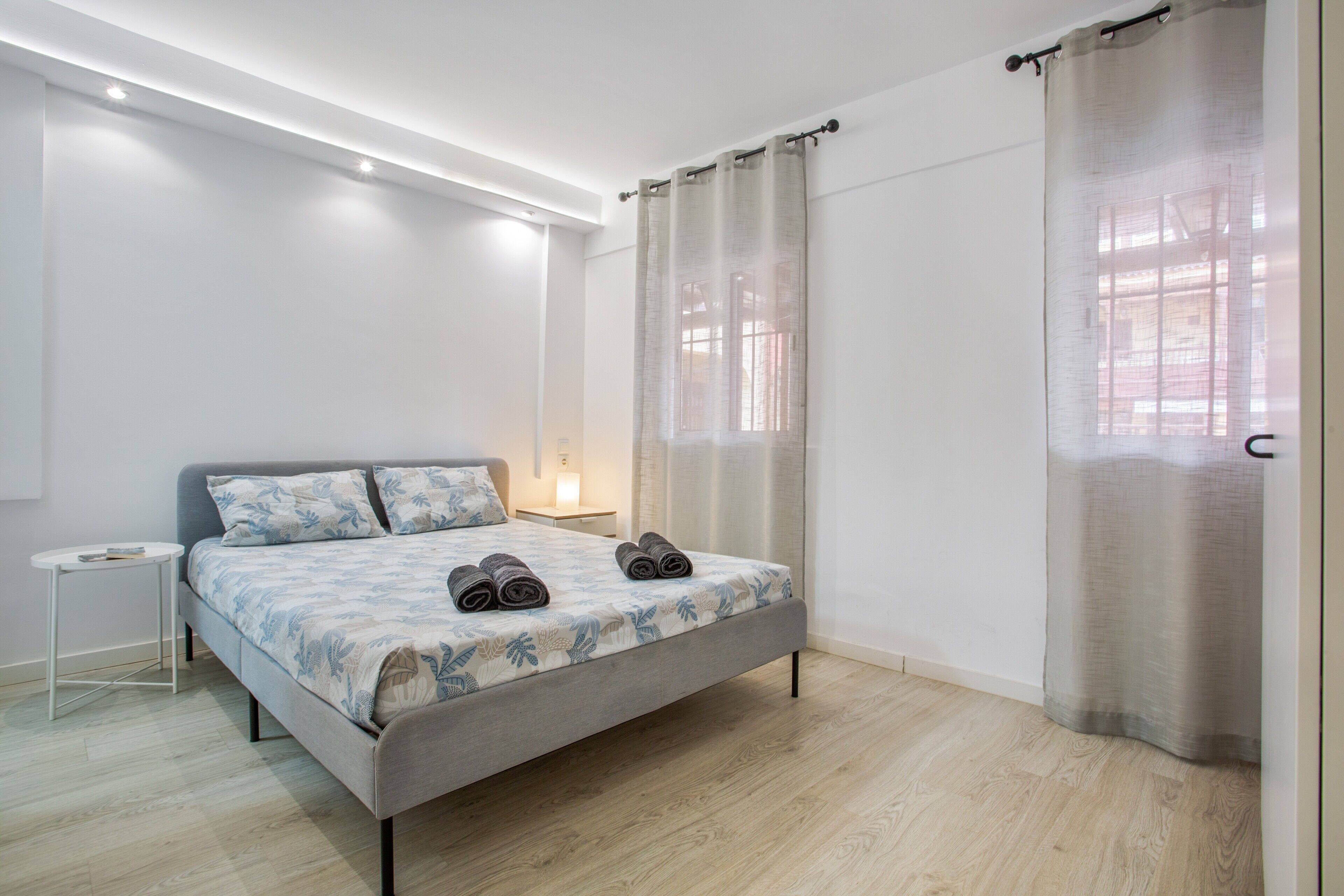 Een moderne slaapkamer met een bed, nachtkastje en een raam met gordijnen.