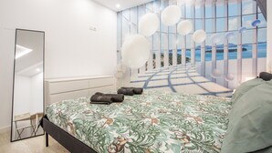 A modern bedroom with a large bed, a mirror, and a view of the sea through a window. - Vacation Home 'Las Américas Seafront - Free Wi-fi' with Private Terrace, Wi-Fi and Air Conditioning (Playa de la Américas)