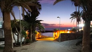 A paved pathway lined with palm trees leading to a beach at dusk. - Vacation Home 'Las Américas Seafront - Free Wi-fi' with Private Terrace, Wi-Fi and Air Conditioning (Playa de la Américas)