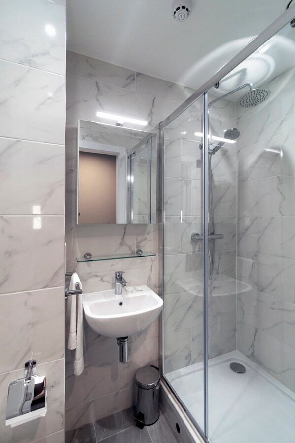 A modern bathroom with a glass-enclosed shower, a white sink, and a marble-tiled wall. - Queen Street Place (Galway)