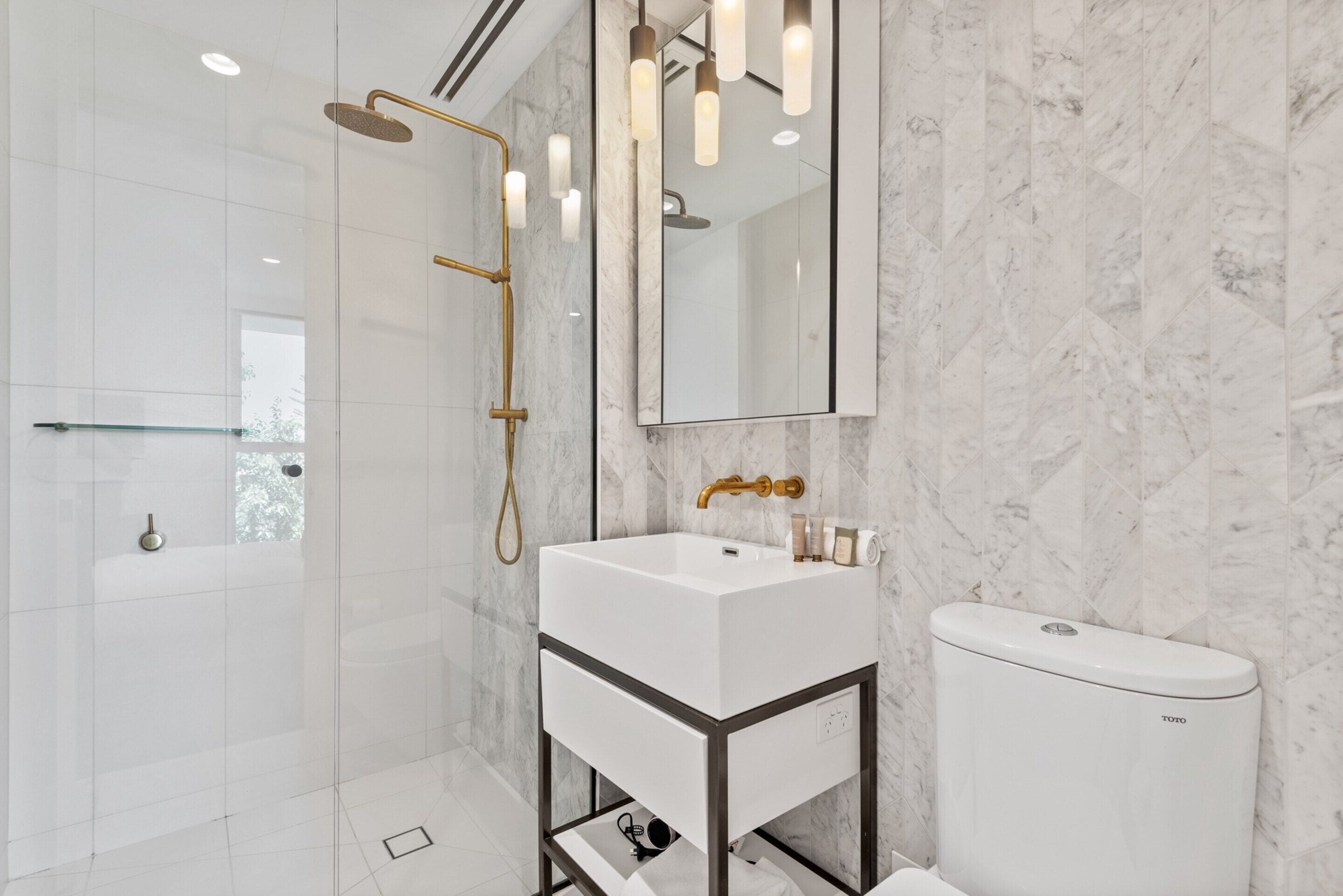 A modern bathroom with a white sink, a toilet, and a shower with a gold showerhead.