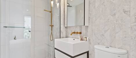 A modern bathroom with a white sink, a toilet, and a shower with a gold showerhead.