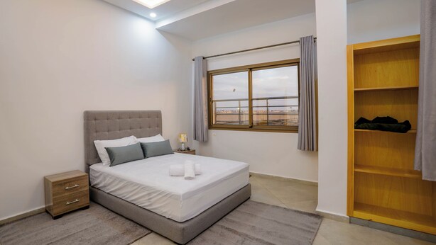 A modern bedroom with a large bed, a nightstand, a wooden wardrobe, and a window with curtains. - Residence fakir (Dakhla)
