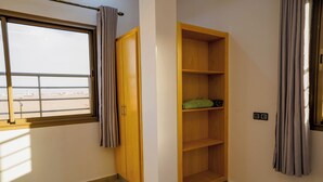 A room with a large window, a wooden wardrobe, and a built-in shelving unit. - Residence fakir (Dakhla)