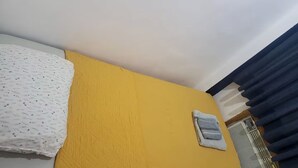 Een kamer met een gele muur, een wit bed met een bloemenprintdeken en een handdoek aan de muur.