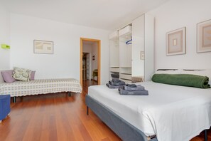 Een slaapkamer met een bed, een bankje, een kledingkast en een deur naar een andere kamer.