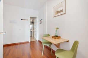 Een kamer met een houten vloer, een tafel met stoelen, een bloemenvaas en een lijst met een foto aan de muur.