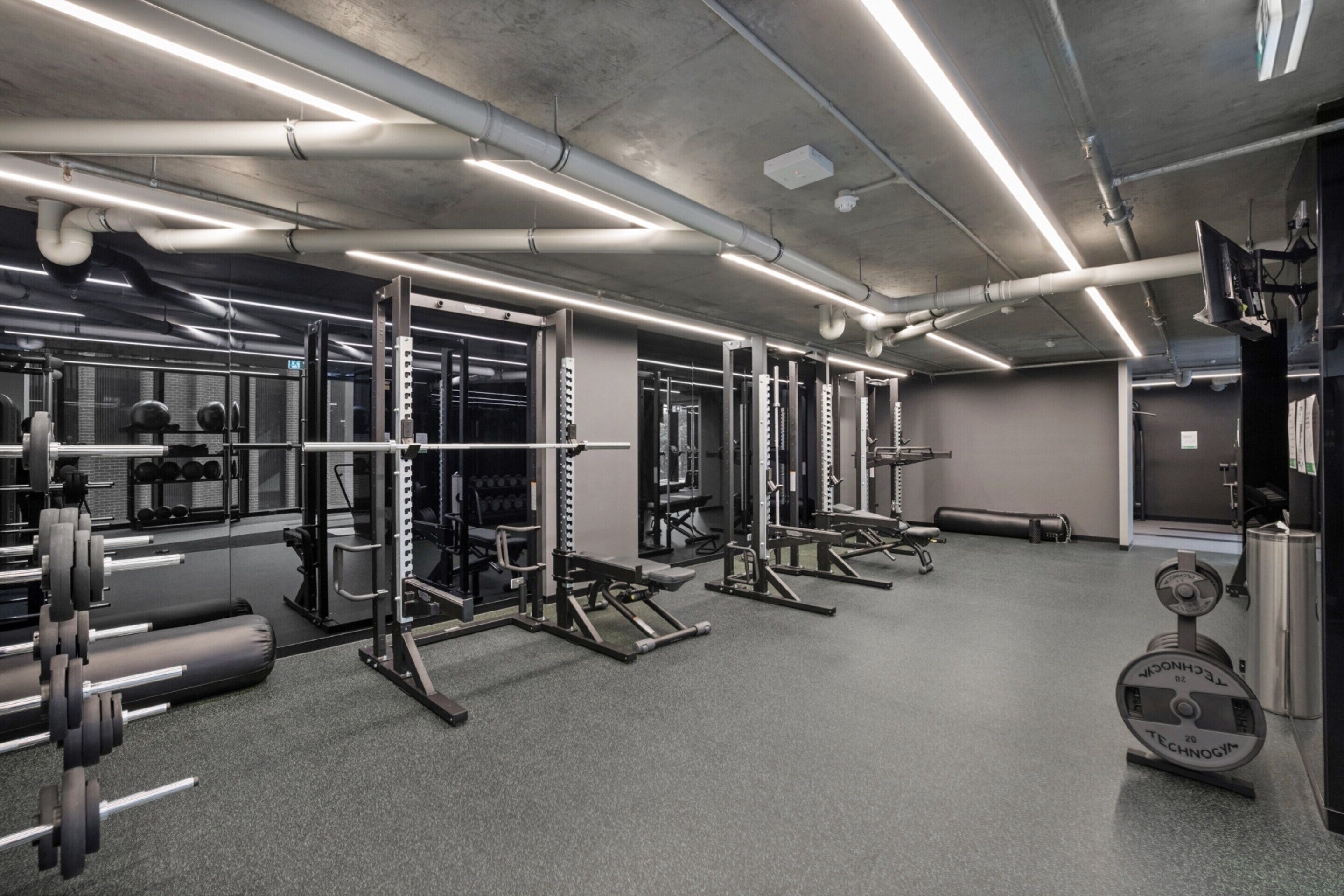 Een sportschool met diverse gewichthefbenches, inclusief bankjes, squatsystemen en dumbbells.