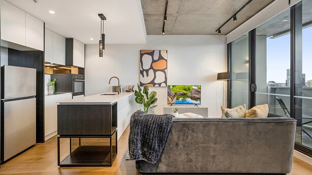 Una cocina moderna con una isla central, un sofá gris con cojines y un ventanal con vistas a la ciudad.