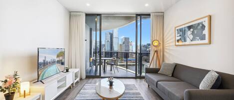 Una sala de estar moderna con un sofá, una mesa de centro, un televisor y un balcón con vistas a la ciudad.