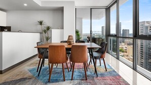 A modern dining area with a wooden table and chairs, a colorful rug, and large windows offering a city view. - Central 2-bed With Parking & Stunning Views (Sydney)