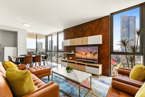 Uma sala de estar moderna com uma televisão grande, sofás de couro, uma mesa de centro e vista para a cidade.