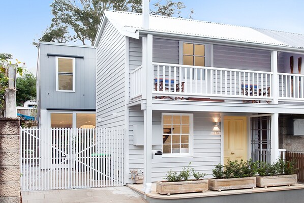 Une maison à deux étages avec un balcon, une porte d’entrée et une cour clôturée.