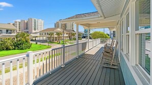 A wooden deck with a railing, a covered porch, and a view of surrounding buildings. - A Block Away- 5 BR/3BA- Dog Friendly- Pool (North Myrtle Beach)