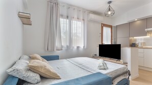 Una habitación moderna con cama, televisor, zona de cocina y ventana con cortinas.