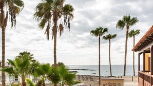 Vista costera con palmeras, una playa y un edificio con un letrero que dice 'La Grotta Ristorante - Pizzeria'.