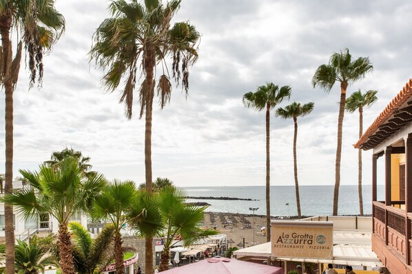 Une vue sur la côte, avec des palmiers, une plage et un bâtiment sur lequel on peut lire l’inscription : « La Grotta Ristorante - Pizzeria ».